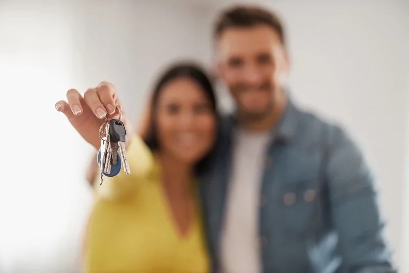 Wohnungsschlüssel Pärchen unscharf im Hintergrund, Mann hält Schlüssel in der Hand, hierauf ist der Fokus.