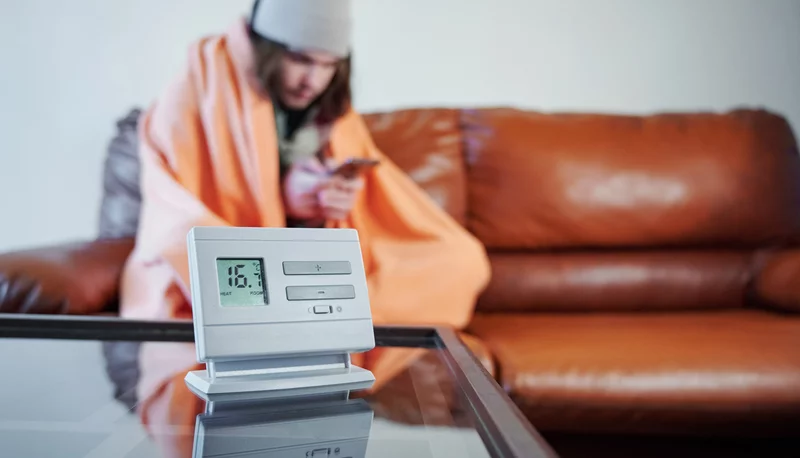 Kälte in der Wohnung Frau sitzt in Decke eingewickelt auf dem Sofa. Im Vordergrund zeigt ein Termometer 16 Grad